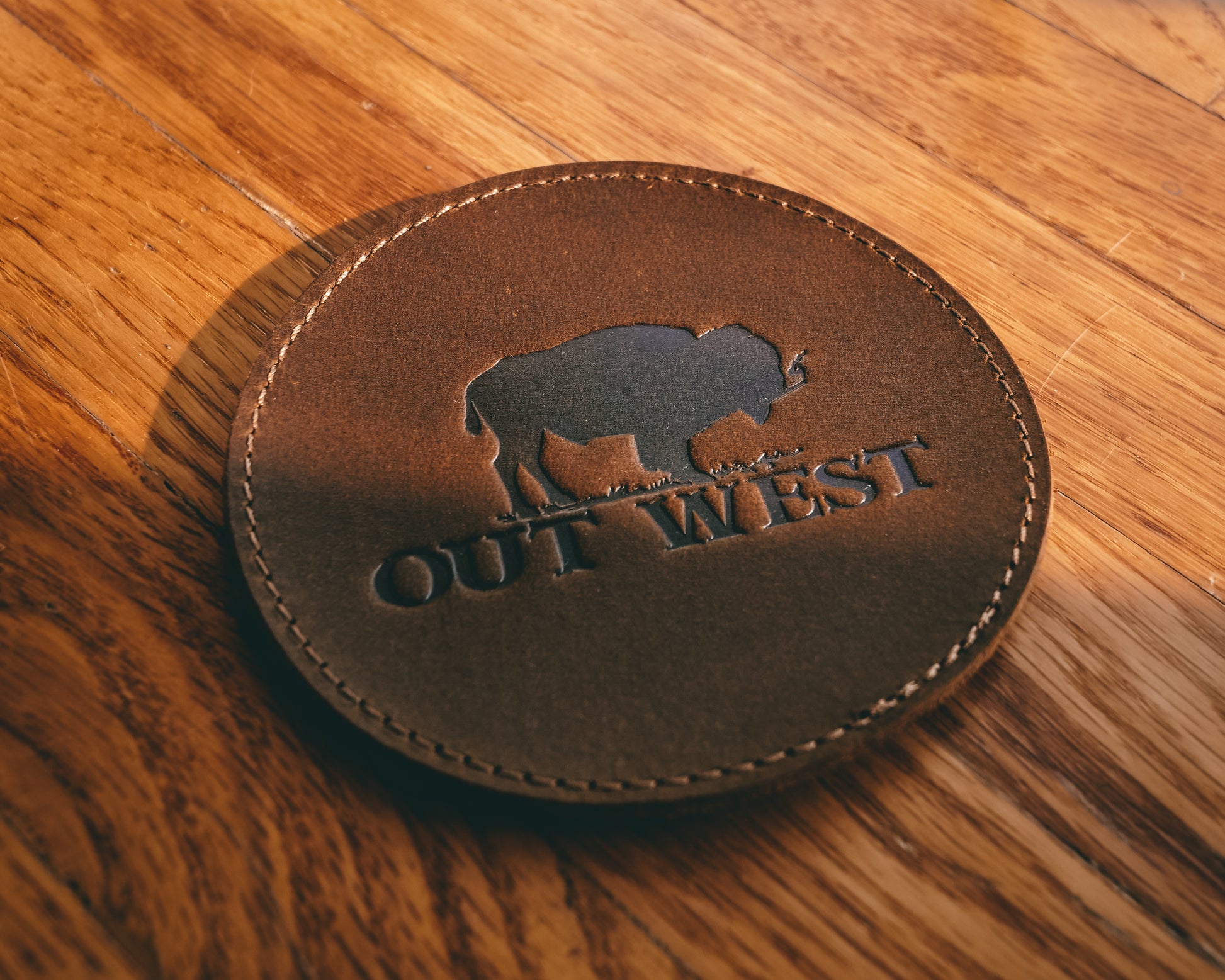 Genuine leather Out West coasters-  Custom designed by Out West and made with genuine leather! Each coaster is branded with the Out West bison logo. Coasters are in a set of 6 + a holder. These coasters will add a true western feel to any home or bar!  Color: Brown  Coaster dimensions: 10cm x 10cm